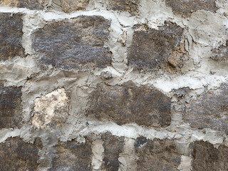 A wall made of stone and cement. The wall is grey and has a few cracks. There are some small holes in the wall