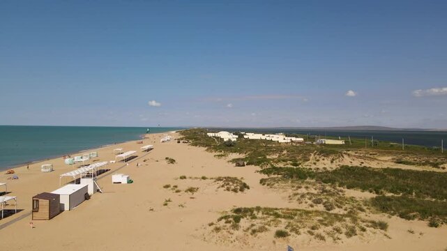 Aerial 4K footage of a sandy beach and emerald Black Sea in Blagoveschenskaya, Russia. Shows coastline, bathers, boats, and beach facilities.