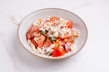 Fresh tomato salad with herbs and cheese in a white bowl