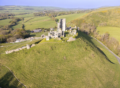 Aerial view of the majestic ruins of Corfe Castle stand proudly atop a verdant hill, a stark contrast to the surrounding lush, rolling fields, Wareham, England, United Kingdom.