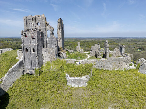 Aerial view of the ancient ruins of Corfe Castle stand proudly atop a verdant hill under a clear blue sky, Wareham, England, United Kingdom.