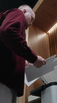Vertical low angle shot of Caucasian male manager doing copies of documents on multifunction printer in office space