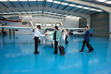 Flight instructor shaking hands with businesswoman in aircraft hangar