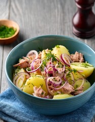 Potato sald with fresh herbs , tuna and red slcied onions in a pale blue ceramic bowl on gray wooden table. Generated image