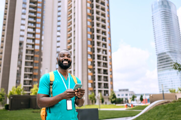 Male black nurse standing outside urban buildings while using a smartphone during daytime