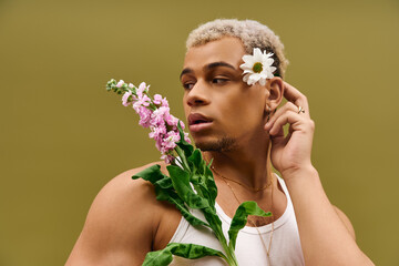 Stylish young man in tank top among vibrant flowers in a studio