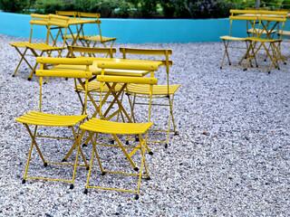 yellow chairs and round tables in a cafe on a cobbled square with a sand surface of compacted...