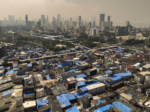 Aerial view of a stark contrast between the dense, blue-roofed shanties and the towering skyscrapers, a testament to urban disparity, Dharavi,Mumbai, Maharashtra, India.