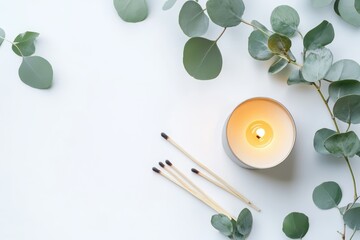 lit candle with eucalyptus greenery and matches on white background.