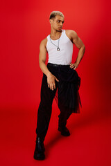 Confident young man showcases trendy fashion against vibrant red backdrop in studio