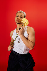 Young man showcases trendy style in red studio with vibrant flower