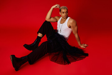 Young stylish man showcases trendy fashion in vibrant red studio setting