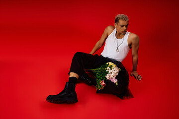 Handsome young man in a red studio showcasing trendy fashion style with flowers