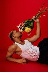 Young man showcases bold style with flowers in a vibrant red studio setting