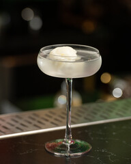 A light-colored alcoholic cocktail with a scoop of white sorbet or ice cream is presented in a...