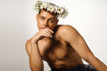 Muscular young man with dyed hair and floral crown poses beautifully in studio setting