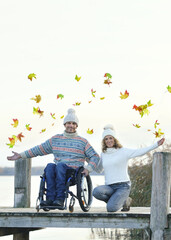 A Man in a Wheelchair and His Girlfriend Throwing Colorful Leaves on an Old Wooden Pier by the Lake