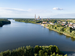Aerial view of the Basilica of Our Lady of Lichen surrounded by lush forest, lake, and rural landscape under clear blue summer sky. Shot in Poland