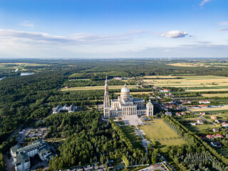 Aerial view of the Basilica of Our Lady of Lichen surrounded by lush forest, lake, and rural landscape under clear blue summer sky. Shot in Poland