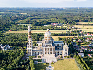 Aerial view of the Basilica of Our Lady of Lichen surrounded by lush forest, lake, and rural landscape under clear blue summer sky. Shot in Poland