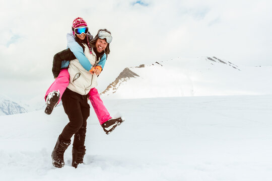 Joyful young loving couple walk piggyback smiling in deep snow share romantic bonding on snowy mountain, love, happiness, freedom, playful relationship, romantic adventure, carefree winter escape