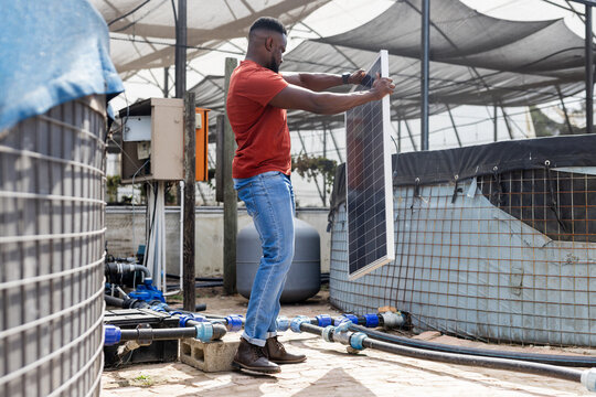 Installing solar panel in nursery, African American technician handling tanks, pipes and cabinet