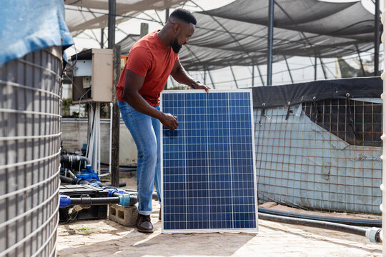 Technician in red shirt and blue jeans is lifting solar panel inside shaded water pumping station