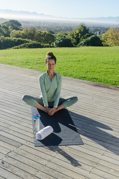 Senior woman holding butterfly pose on wooden deck in athletic wear with towel, water bottle
