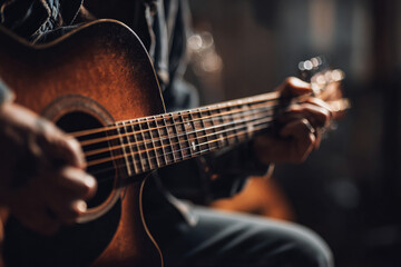 Obraz premium Close-up of musician’s hands tuning acoustic guitar in softly lit studio, woodgrain and metallic strings visible