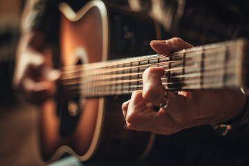 Fototapeta premium Close-up of musician’s hands tuning acoustic guitar in softly lit studio, woodgrain and metallic strings visible