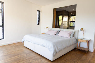Upholstered bed resting with pink pillows and brass lamps glowing beside windows revealing greenery