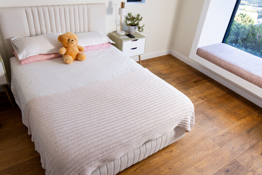 Bedroom showcasing well-made bed with white sheets and pink throw, teddy bear resting on pillows