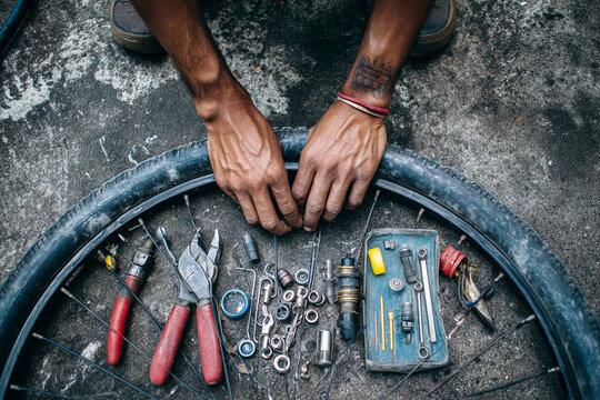 Top view of two hands fixing bicycle inner tube, tools spread out on concrete floor, grease marks and rubber patches visible