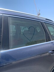 Heart drawn on the dusty side window of a car parked outside a construction site