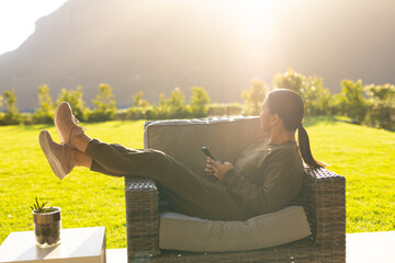 Fototapeta premium Wicker armchair resting on sunlit patio overlooking lawn and hills, with succulent resting on table
