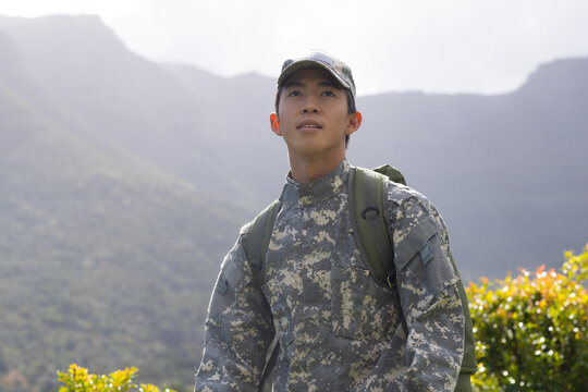 Asian man standing in mountain valley wearing camouflage uniform with cap and olive drab backpack