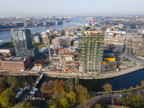 Aerial view of a vibrant tapestry of construction sites, waterways, and autumnal trees paints a picture of urban development, Amsterdam, North Holland, Netherlands.