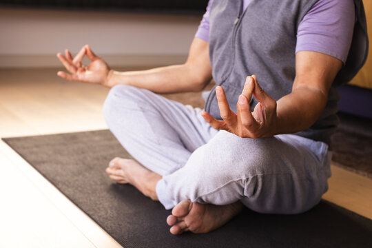Asian man meditating and sitting cross-legged on yoga mat in quiet meditation room with bolster
