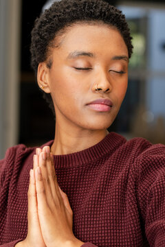 African American woman meditating pressing hands at home wearing nose hoop and hoop earrings