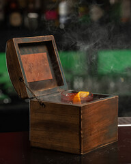 A smoky, dark red alcoholic cocktail with ice and an orange peel garnish is presented in a rocks...