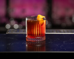 dark red alcoholic cocktail with ice and an orange peel garnish is presented in a rocks glass