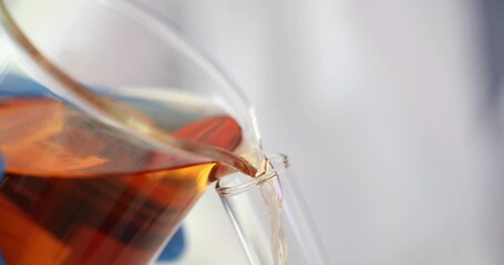 Stream of dark amber liquid reagent pours from large glass beaker into glass test tube. Focus on precise chemical transfer in laboratory setting - Powered by Adobe