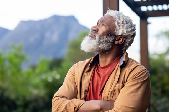 Mature adult African American man standing on wooden porch next to pergola beam, copy space - Powered by Adobe