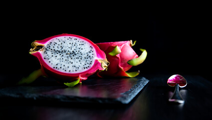 A halved dragon fruit showcases its white flesh and black seeds against a dark backdrop