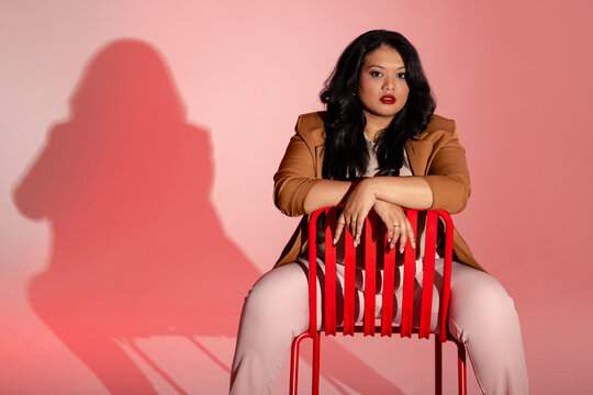 Woman sitting backwards on red chair in portrait studio with pink gradient backdrop casting shadow