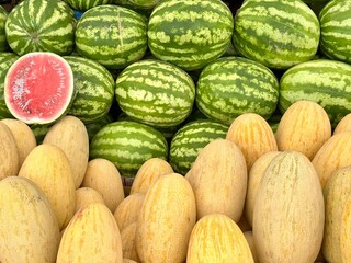 watermelons and melons are beautifully laid out on the counter at the grocery market, one watermelon is cut and shows its juicy core.