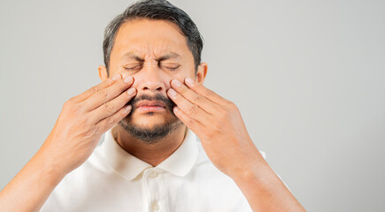 Asian bearded man with eye pain and suffering from eyestrain standing on white background