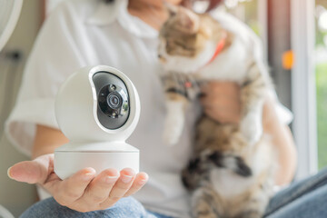A mature woman with a mini security camera for video surveillance of her pet at home.