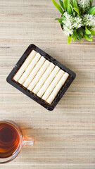 Top view of crispy rolled wafer snack on plastic packaging with a cup of tea isolated on wooden...