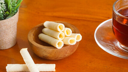 Delicious wafer snack rolls with sweet cheese cream filling serving on plate with a cup of tea...